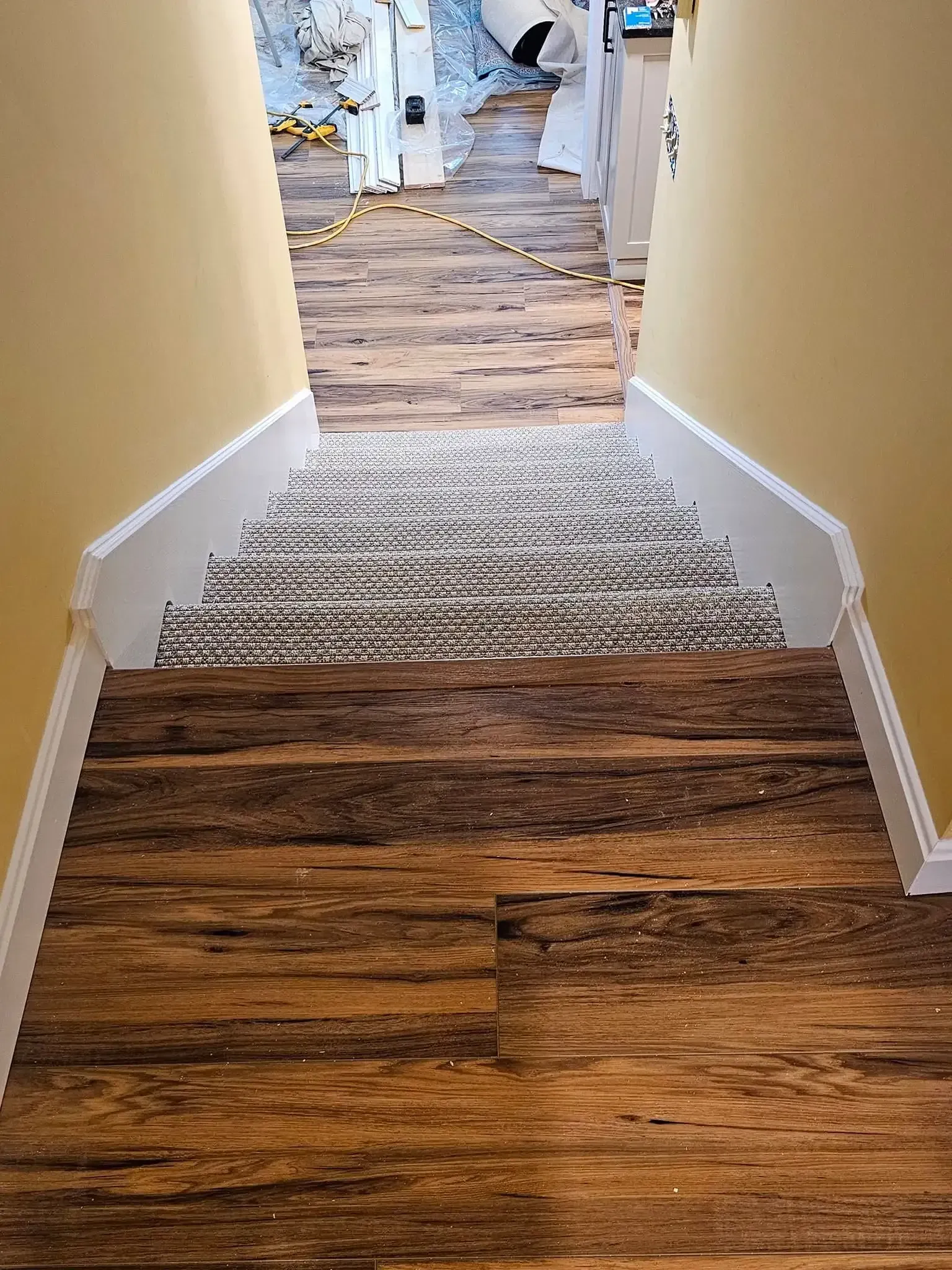 Staircase with wood-look flooring at the bottom, steps with patterned carpet, and view of a room at the top.
