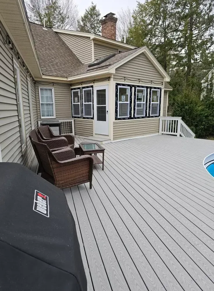 A deck with wicker furniture and a grill next to a house with a sunroom.