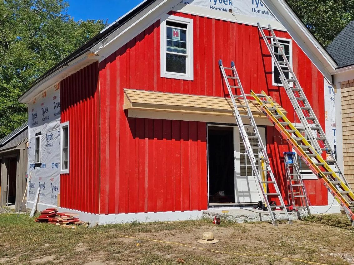 Red-sided building under construction, windows installed, with ladders leaning against it.