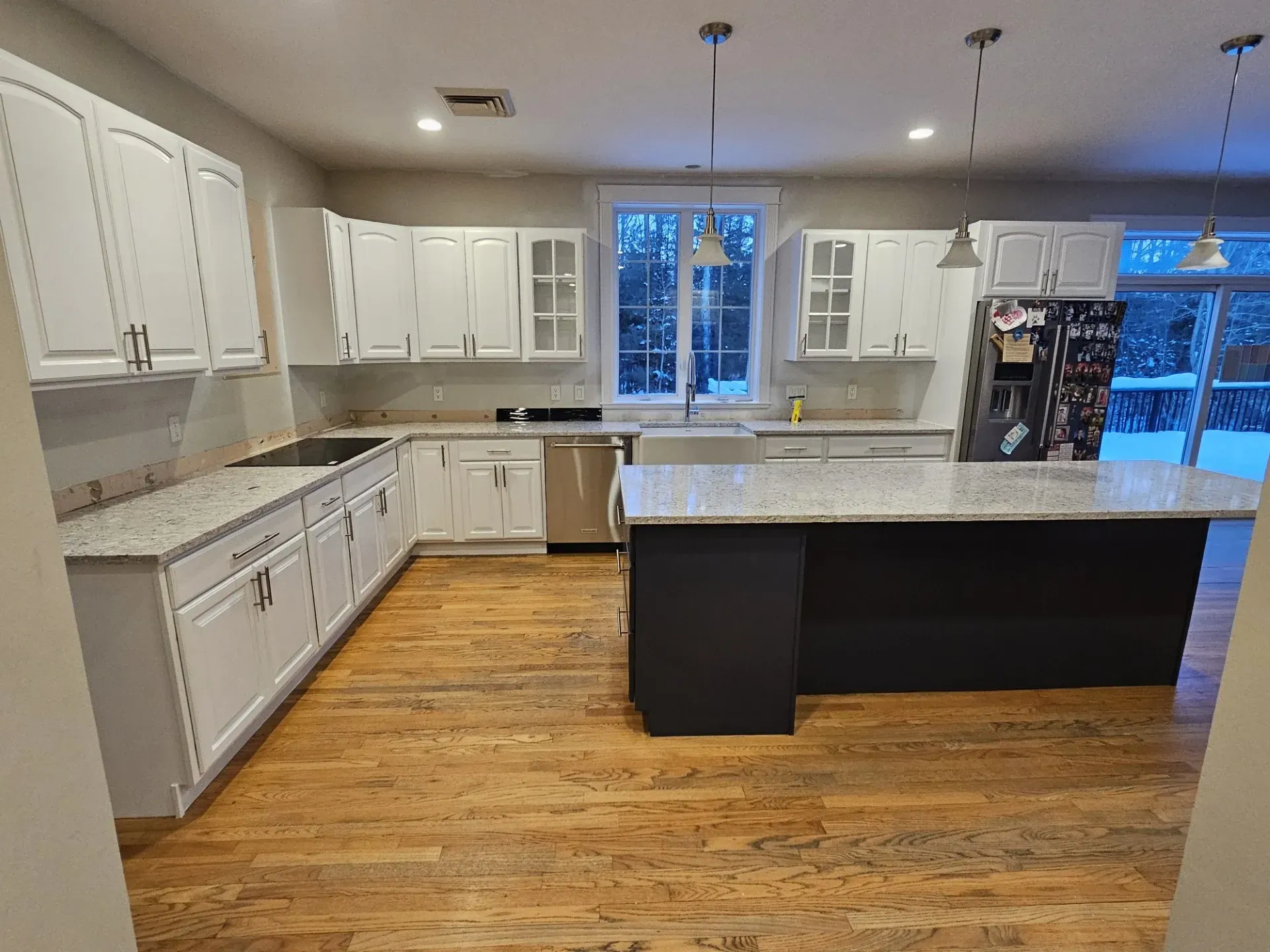 A bright kitchen with white cabinets, granite countertops, a dark kitchen island, and hardwood floors.