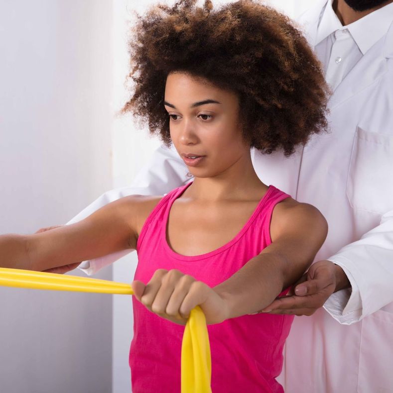 A woman in a pink tank top is doing exercises with a yellow resistance band