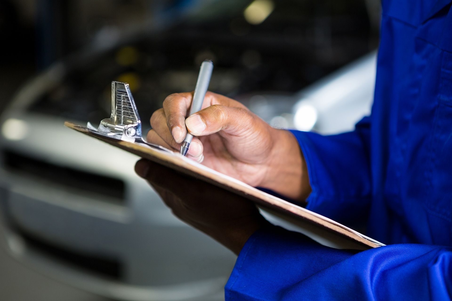 Person in blue uniform writing on a clipboard beside a car