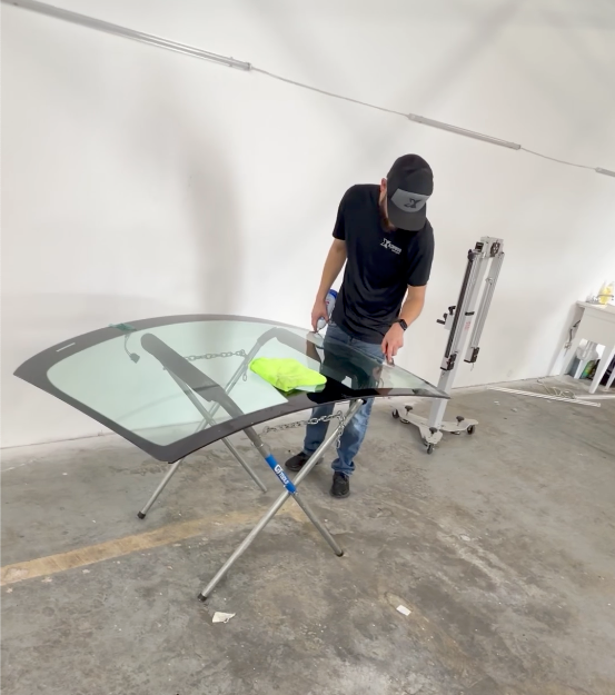 Man working beside a glass table panel in a workshop, with tools and a wheeled stand nearby.