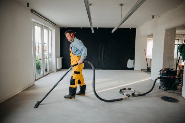 A male cleaner vacuums the inside of a bare building with an orange vacuum.