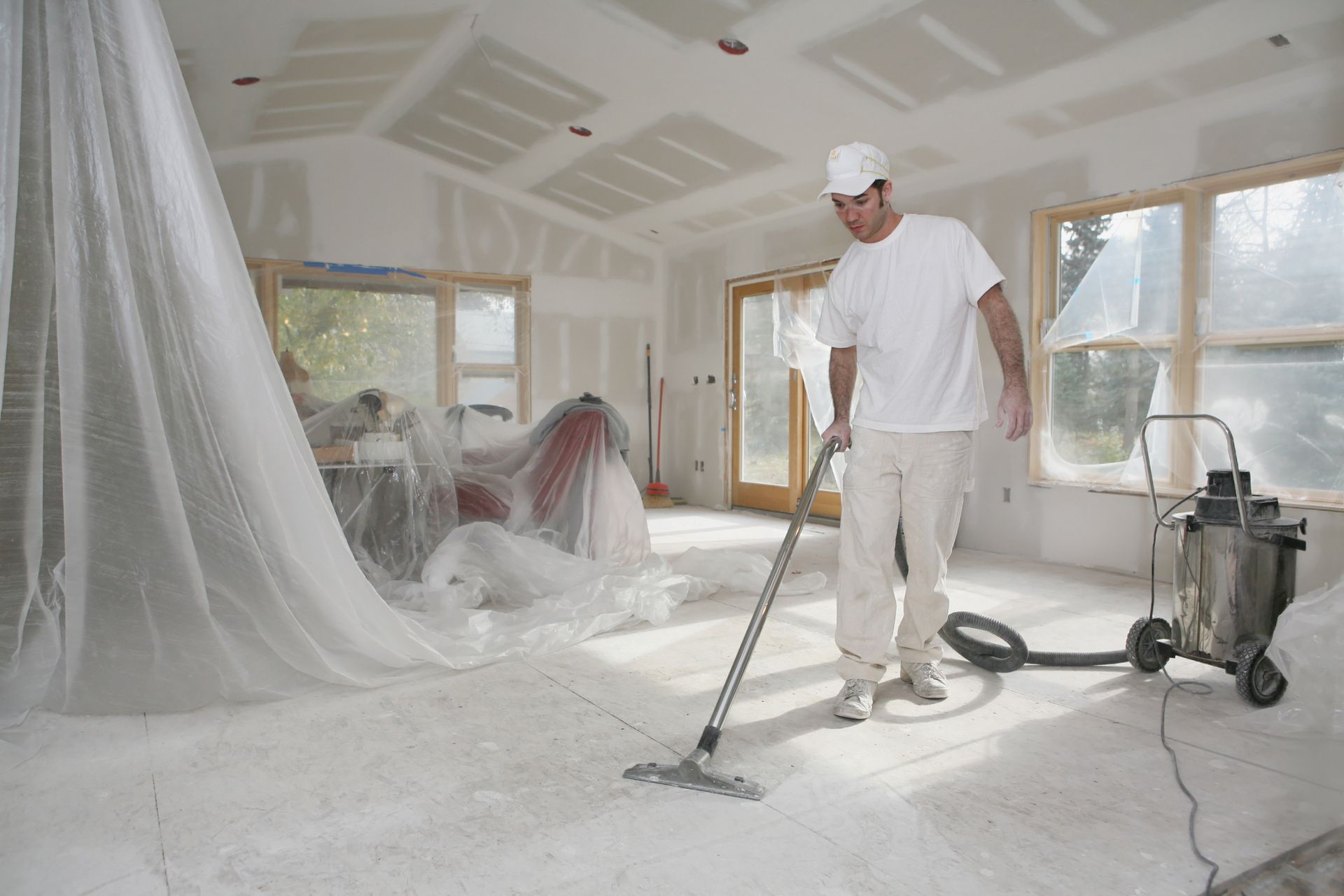 A man in white uniform vacuums the inside of a recently constructed and painted house.