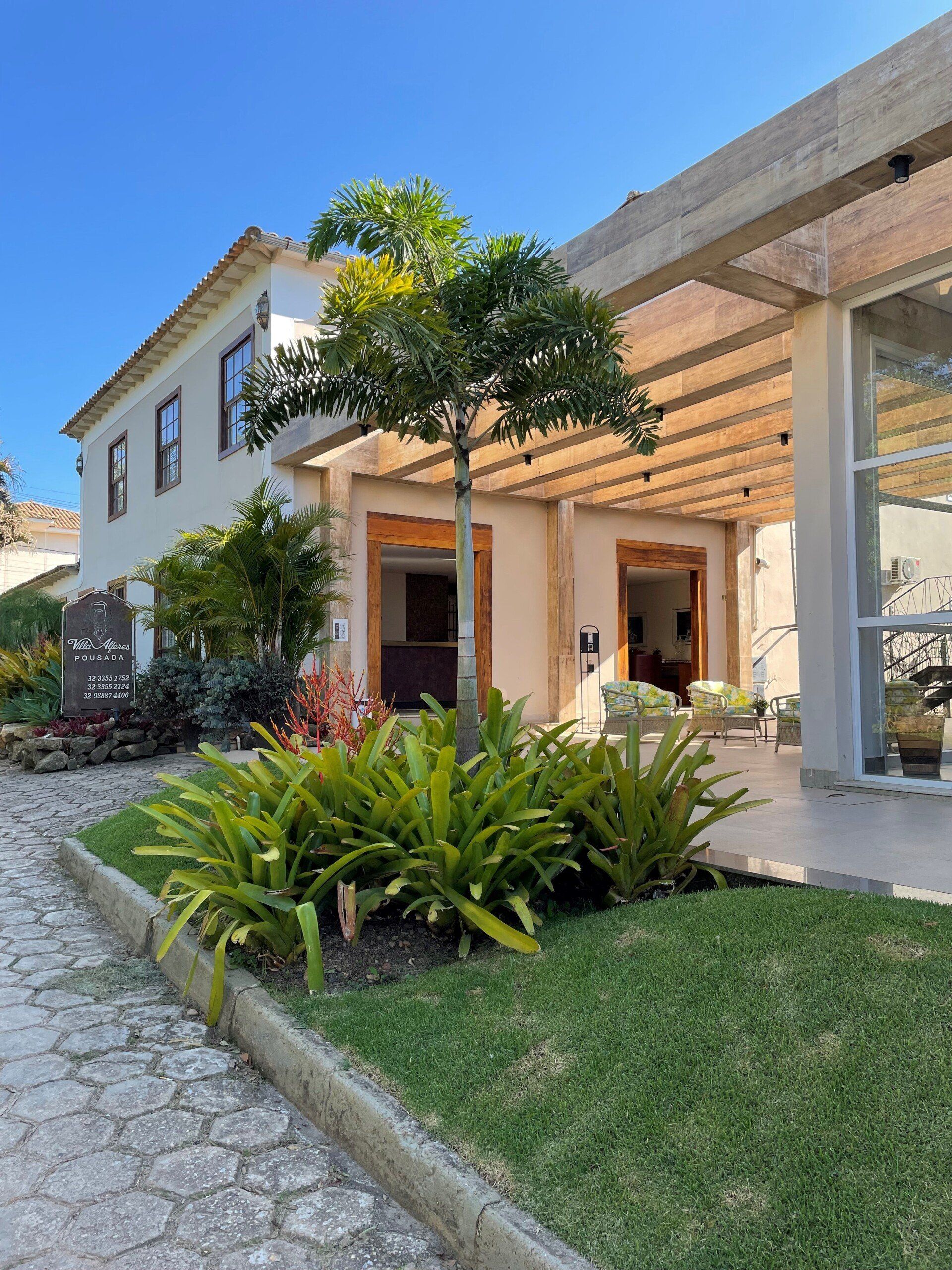 Uma grande casa branca com uma pérgola e uma árvore na frente dela.