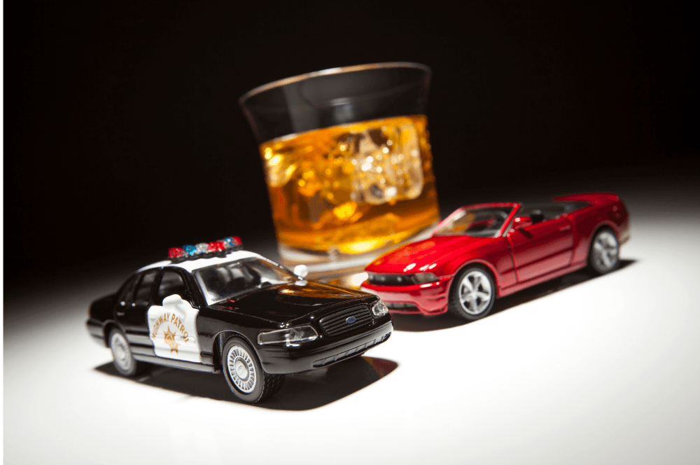 Toy police car and red sports car beside a glass of whiskey on a white surface.