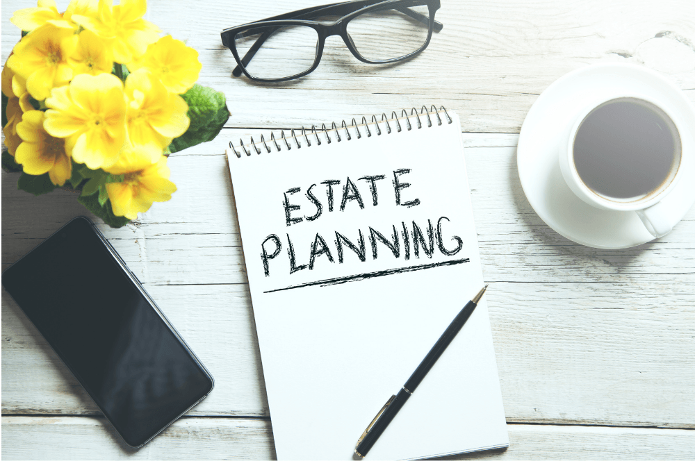 Estate planning notebook on white desk with glasses, coffee, phone, pen, and yellow flowers