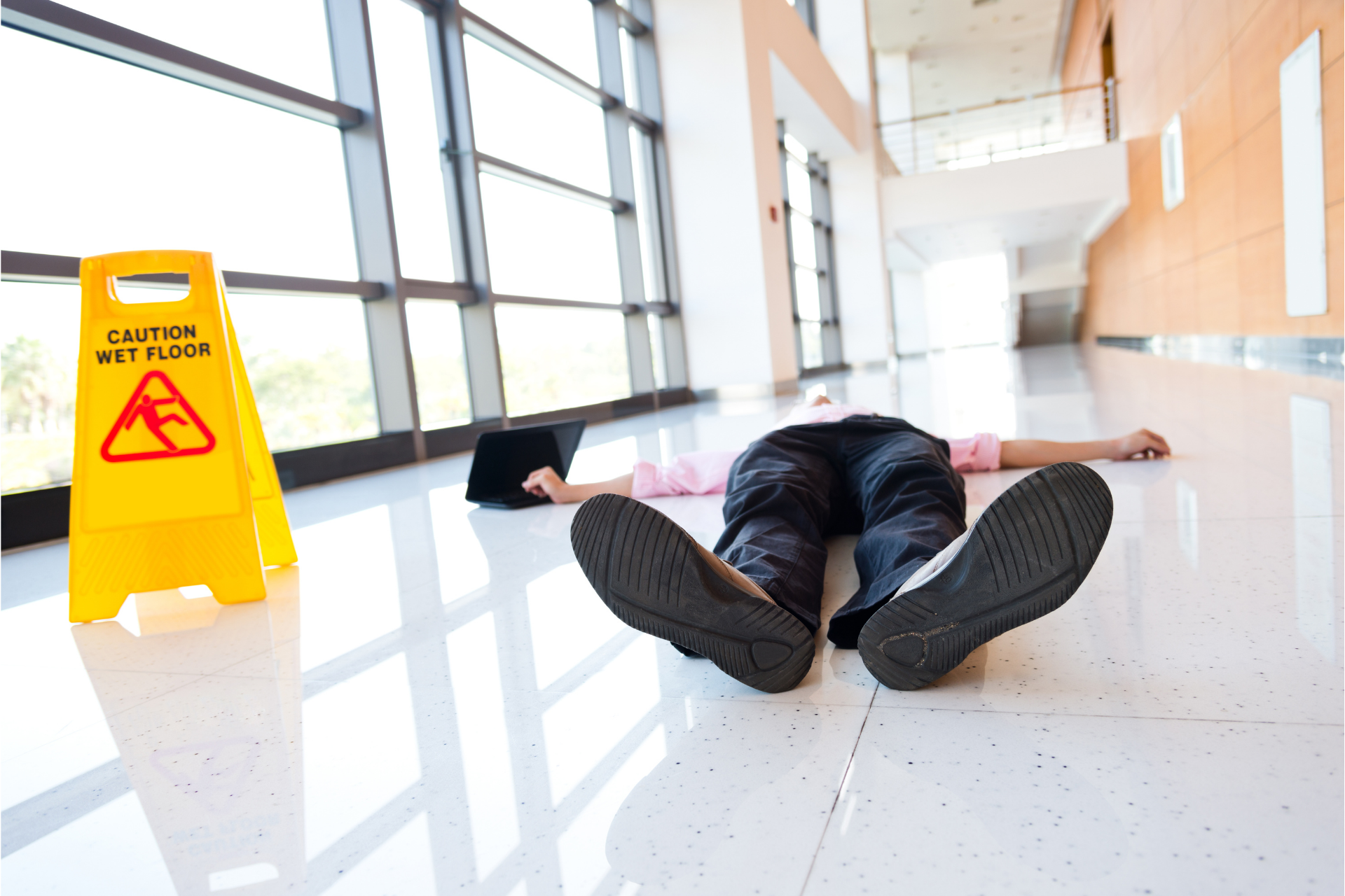 Person lying on a glossy hallway floor near a yellow wet floor caution sign