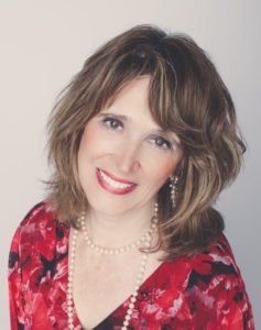 Smiling woman in a red floral top and pearl necklace against a light background