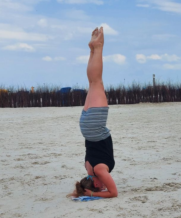 Eine Person macht einen Kopfstand an einem Sandstrand, die Beine gerade nach oben gestreckt