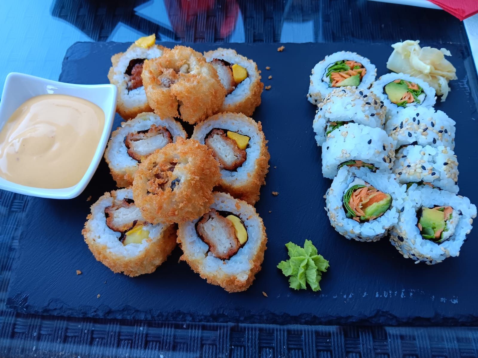 Sushi-Platte mit zwei Sorten Rollen, Wasabi, eingelegtem Ingwer und Dip-Sauce auf schwarzem Schiefer.