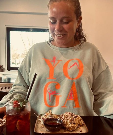 Eine lächelnde Frau betrachtet ihr Essen. Sie trägt ein Sweatshirt mit der Aufschrift „YOGA.