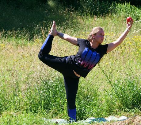 Eine Person balanciert auf einem Bein, hält einen Apfel und beugt sich in einem Feld nach hinten.