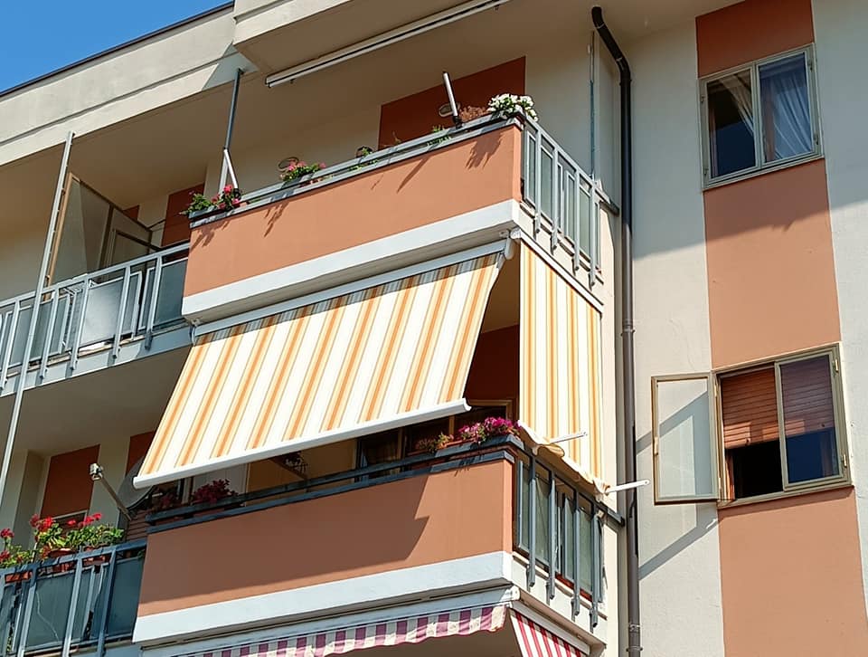 Balconi di appartamenti con tende a righe su un edificio color pesca illuminato dal sole