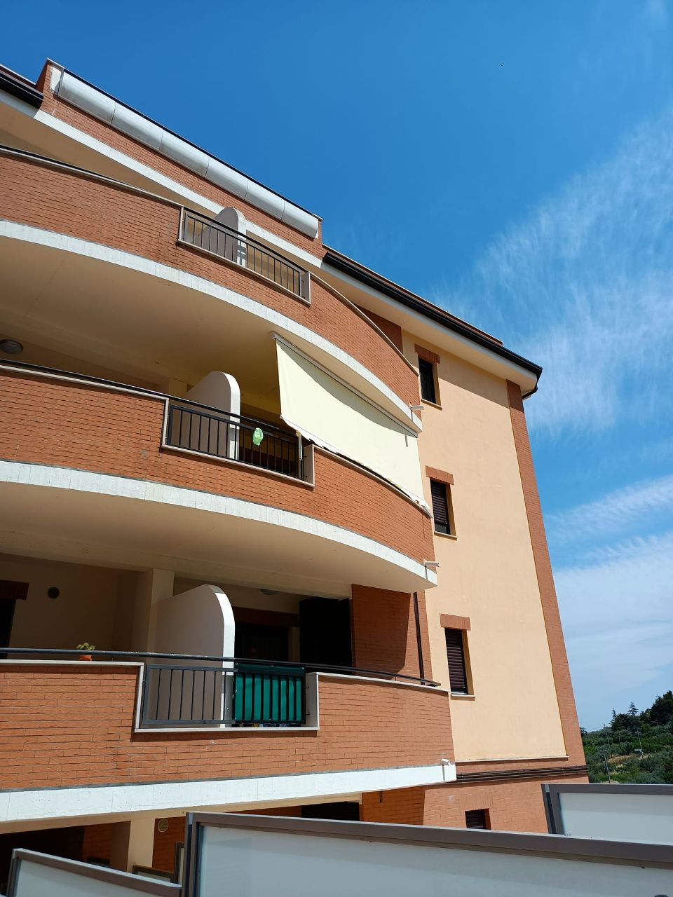 Palazzo residenziale con balconi in mattoni e tende da sole sotto un cielo azzurro