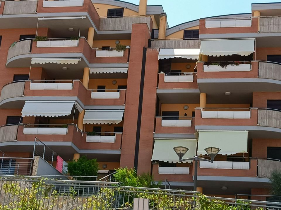 Palazzo residenziale con balconi arancioni e tende da sole bianche, visto dalla strada.