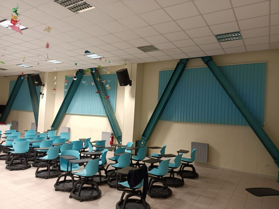 Aula vuota con banchi e sedie color verde acqua, tende dello stesso colore e decorazioni a forma di stella appese al soffitto.
