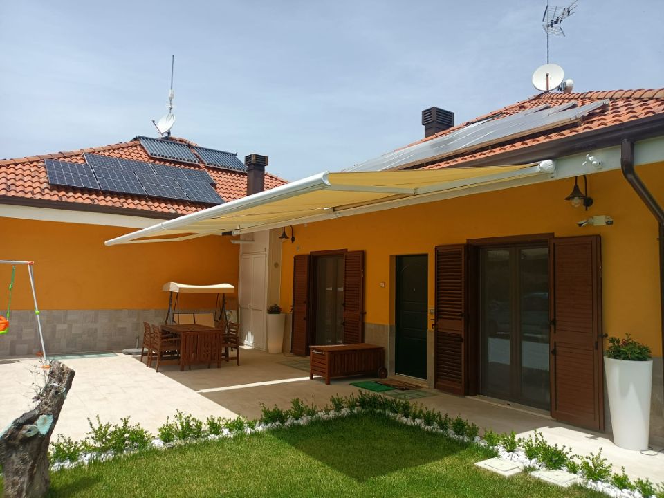 Patio di una casa gialla con tetto di tegole rosse, porte scorrevoli in vetro e piccolo prato verde.