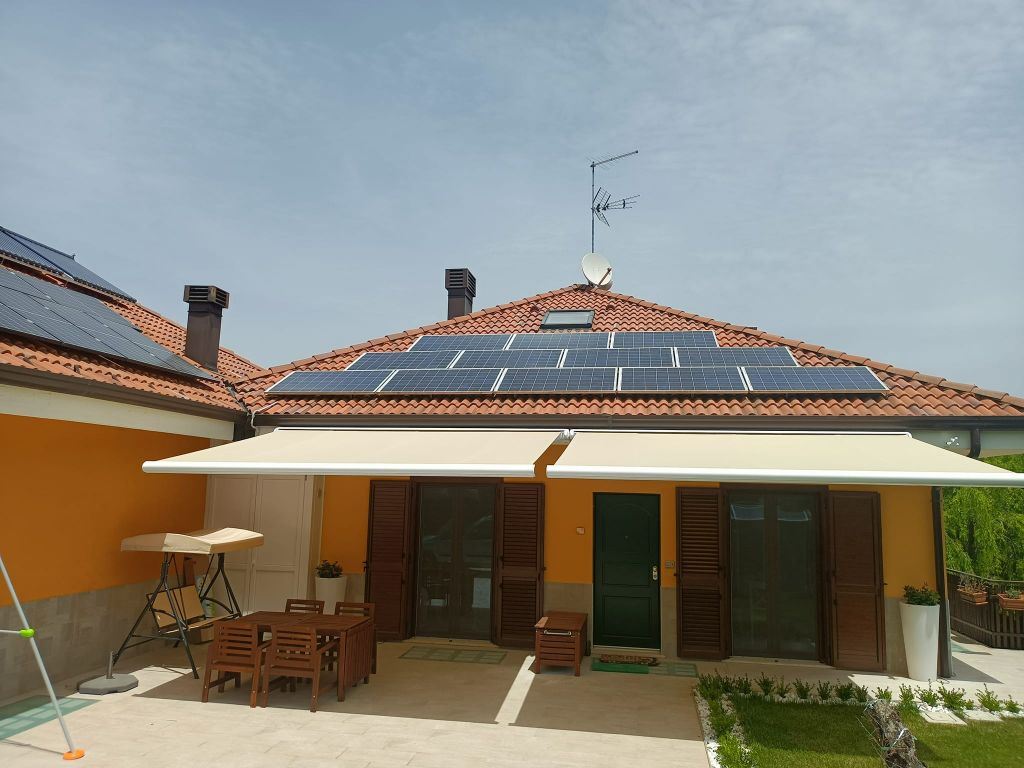 Patio soleggiato di una casa con pareti arancioni, tetto di tegole e mobili da pranzo all'aperto sotto una tenda da sole.