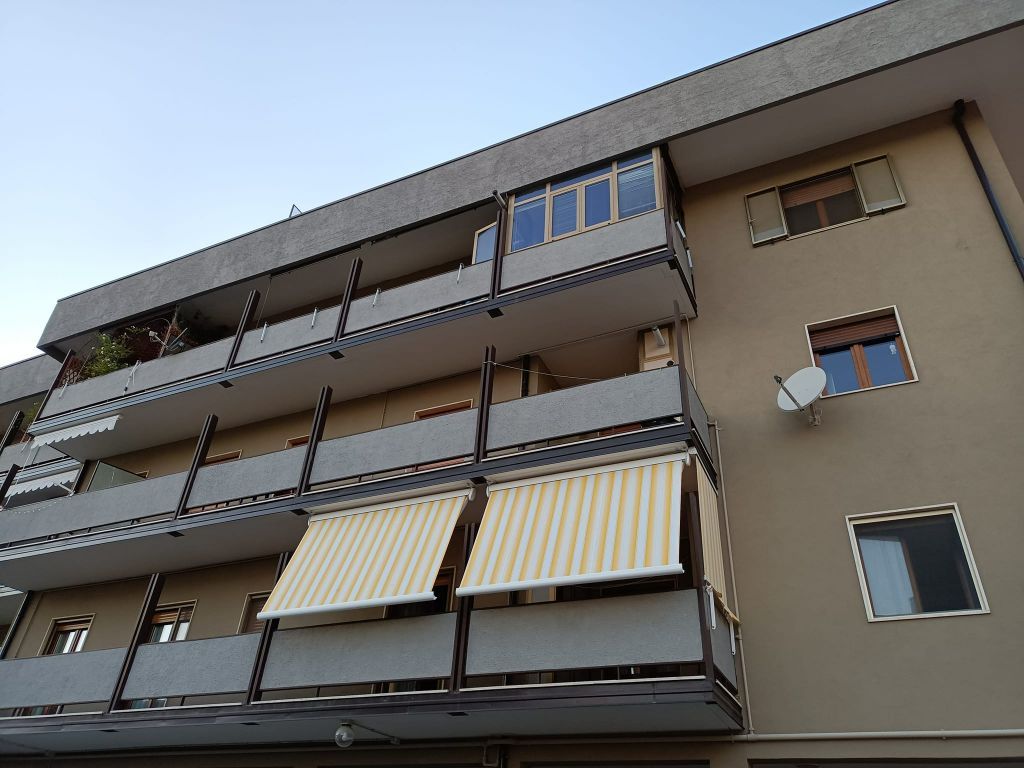 Facciata di un condominio con balconi, tende da sole a righe e finestre contro un cielo azzurro.