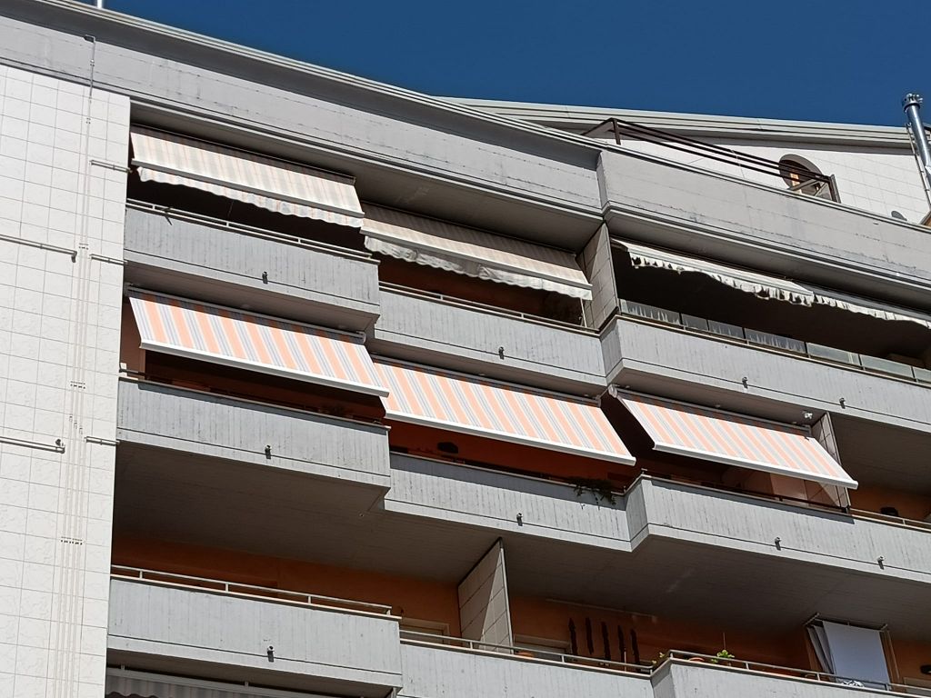 Balconi di appartamenti con ringhiere bianche e tende da sole marroni su un edificio moderno sotto un cielo azzurro