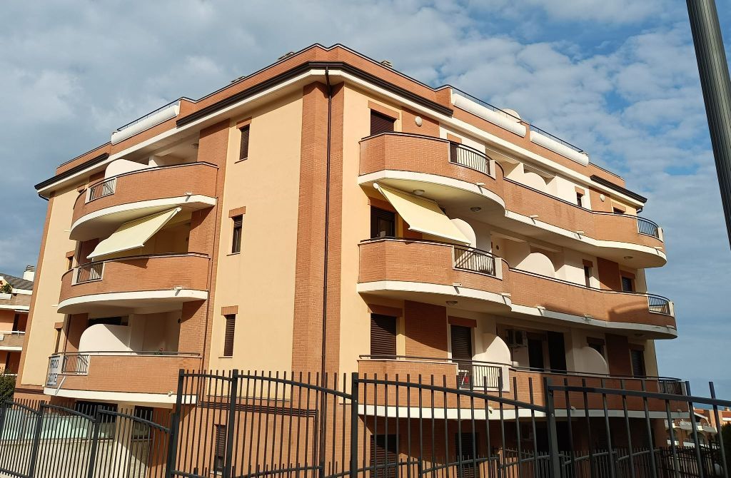 Palazzo di tre piani color pesca con balconi e recinzione nera sotto un cielo azzurro