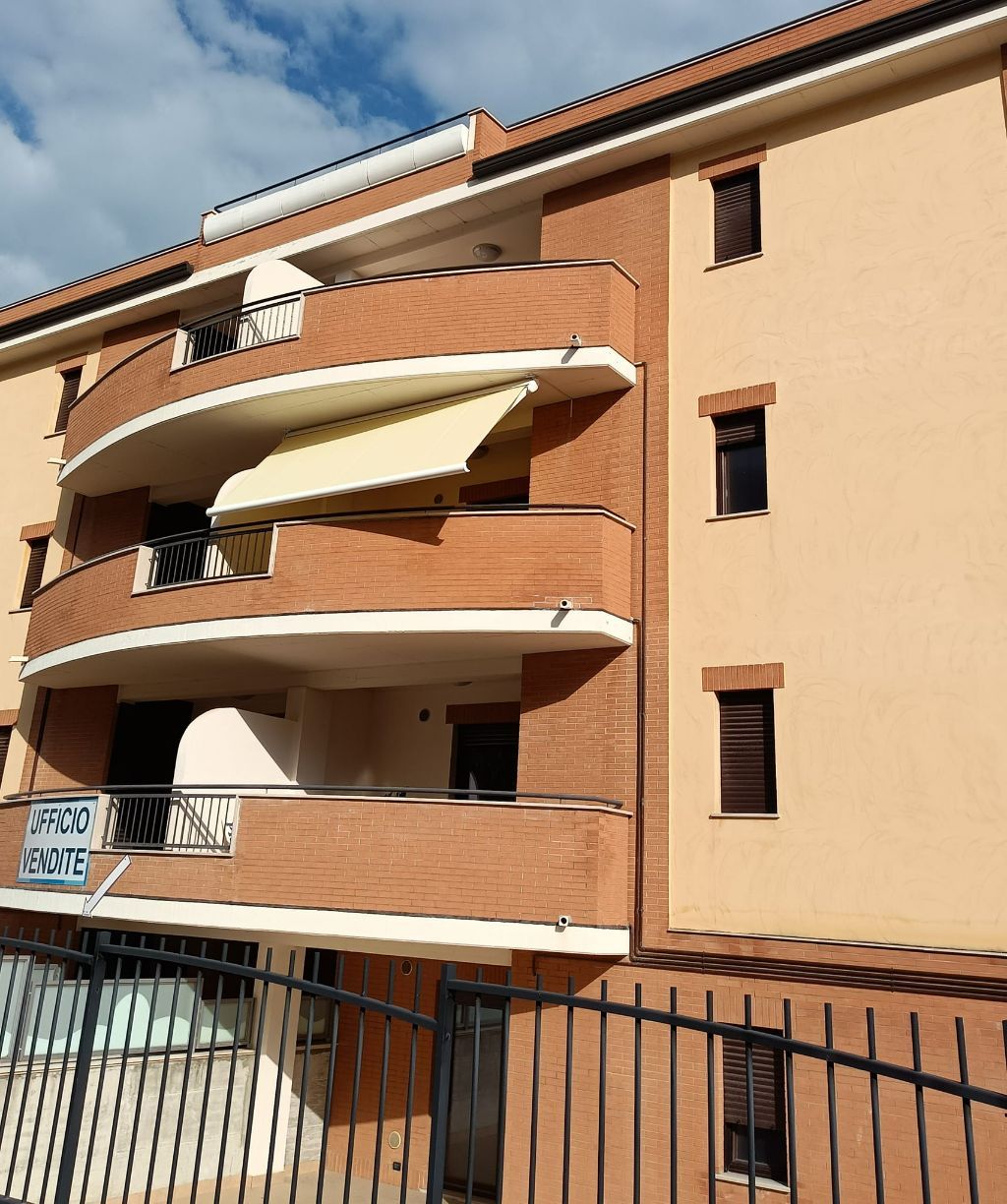 Palazzo residenziale con facciata color pesca e mattoni, balconi curvi e persiane chiuse dietro una recinzione nera.