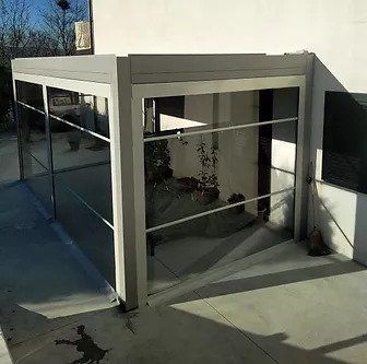 Garage o patio esterno in vetro e metallo con finestre riflettenti e base in cemento.