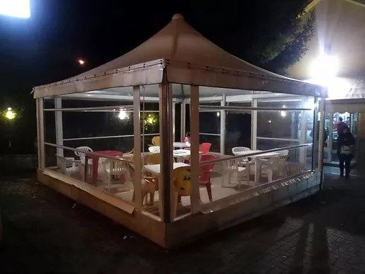Zona pranzo all'aperto allestita con tendone, con tavoli e sedie bianchi illuminati di notte.