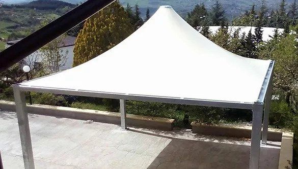 Tenda a baldacchino bianca con tetto a punta su un patio, con alberi e montagne sullo sfondo.