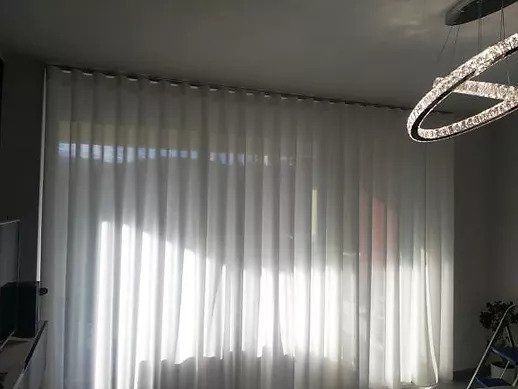 Finestra soleggiata con tende bianche trasparenti in una stanza moderna, lampada a sospensione visibile in alto a destra