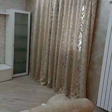 Elegante soggiorno con tende beige a fantasia, uno specchio e un divano bianco trapuntato vicino alla finestra.