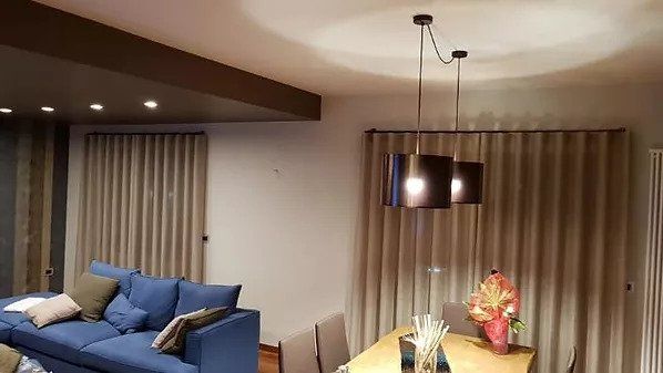 Soggiorno-sala da pranzo moderno con divano blu, tavolo da pranzo, lampade a sospensione e tende beige.