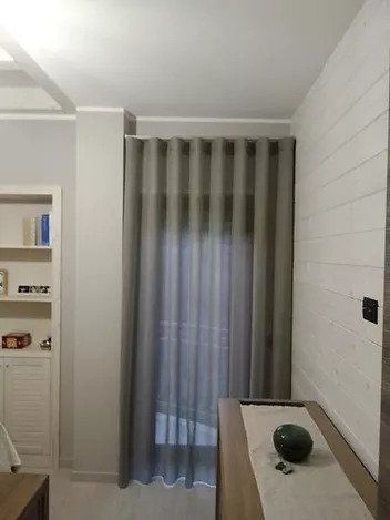 Piccola stanza con tende grigie, scaffali a muro e una scrivania in legno con un oggetto decorativo verde.