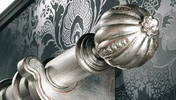 Terminale decorativo argentato su sfondo di tessuto grigio a fantasia.