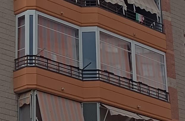 Angolo di un condominio a più piani con tende da sole a strisce e grandi finestre in una giornata nuvolosa.