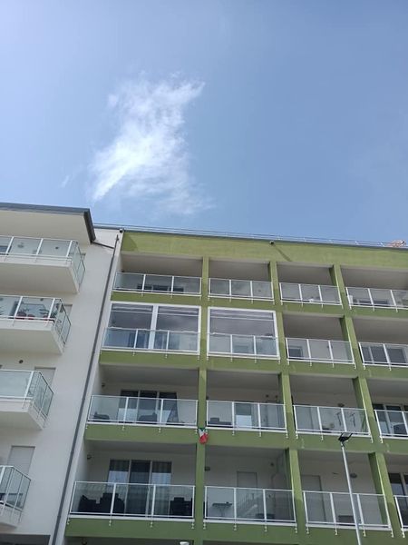 Palazzo residenziale con balconi verdi sotto un cielo azzurro