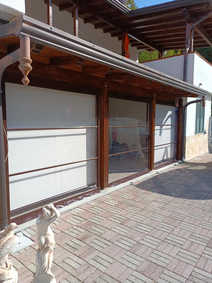 Esterno di un edificio tradizionale con colonne in legno, porte scorrevoli in vetro e patio piastrellato esposto alla luce del sole.