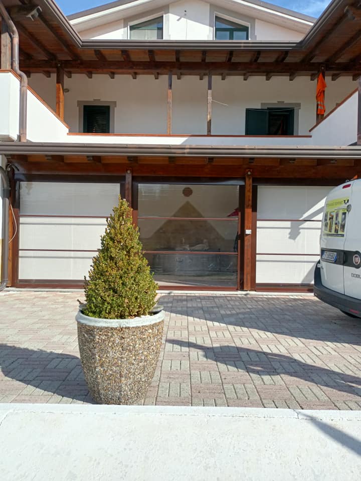 Ingresso principale di una casa con un arbusto sempreverde in vaso e un furgone parcheggiato sulla destra.