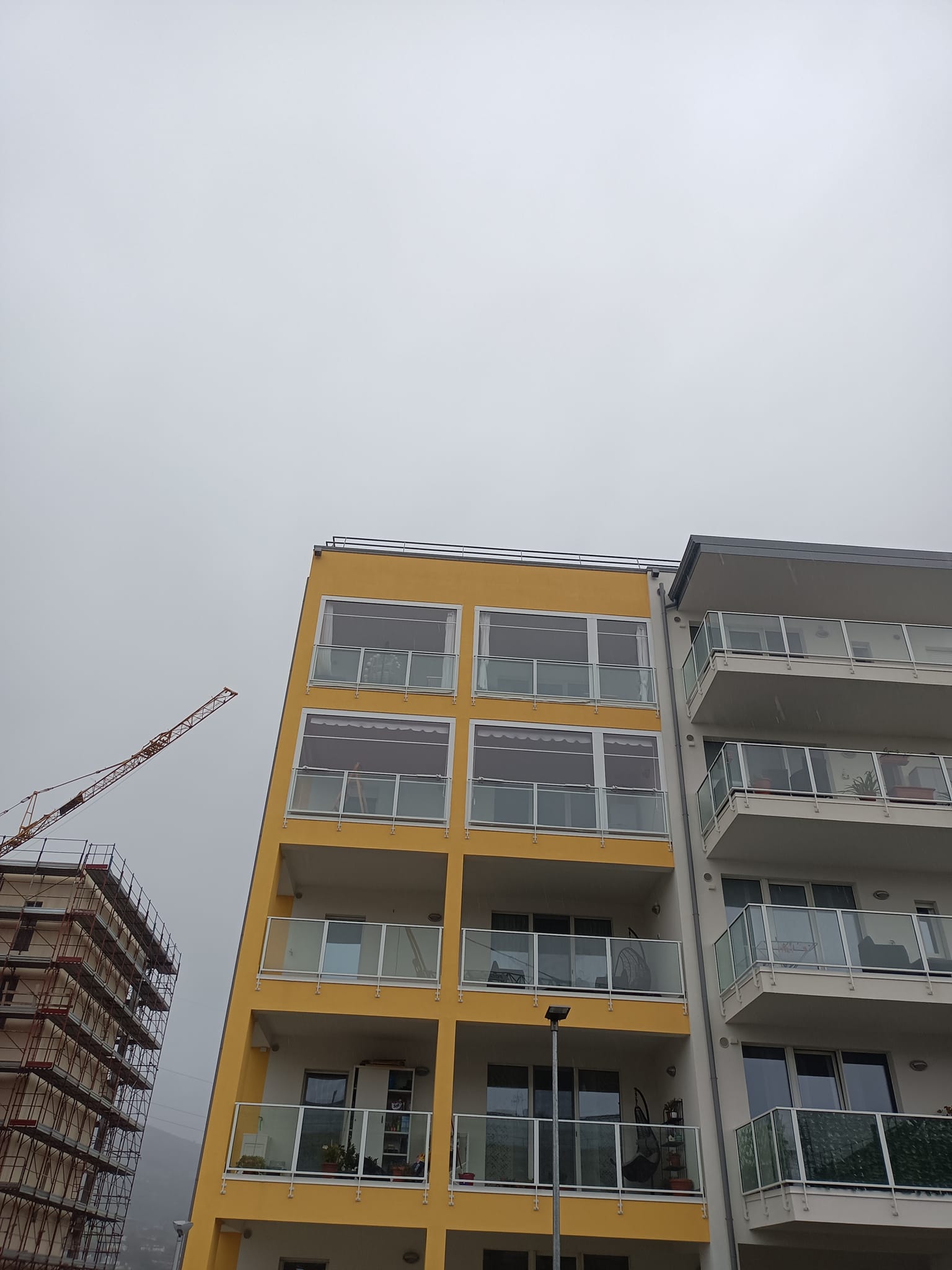 Vista dal basso di un condominio giallo accanto a balconi grigi sotto un cielo nuvoloso.