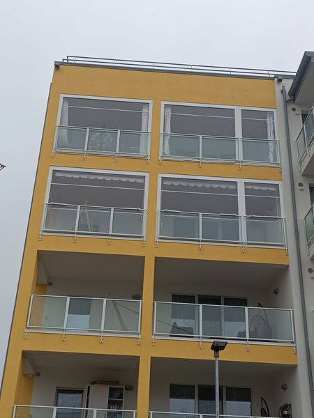 Facciata di un condominio giallo e grigio con balconi e ampie finestre.