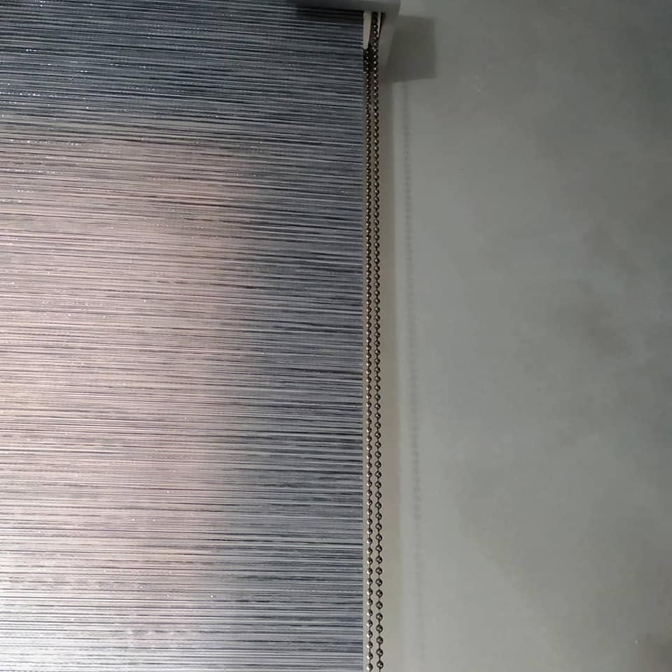 Primo piano di una tenda a rullo grigia chiusa accanto a una parete bianca.