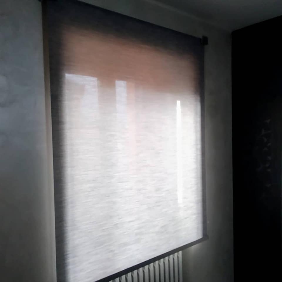 Tenda a rullo bianca chiusa che filtra la luce in una stanza poco illuminata