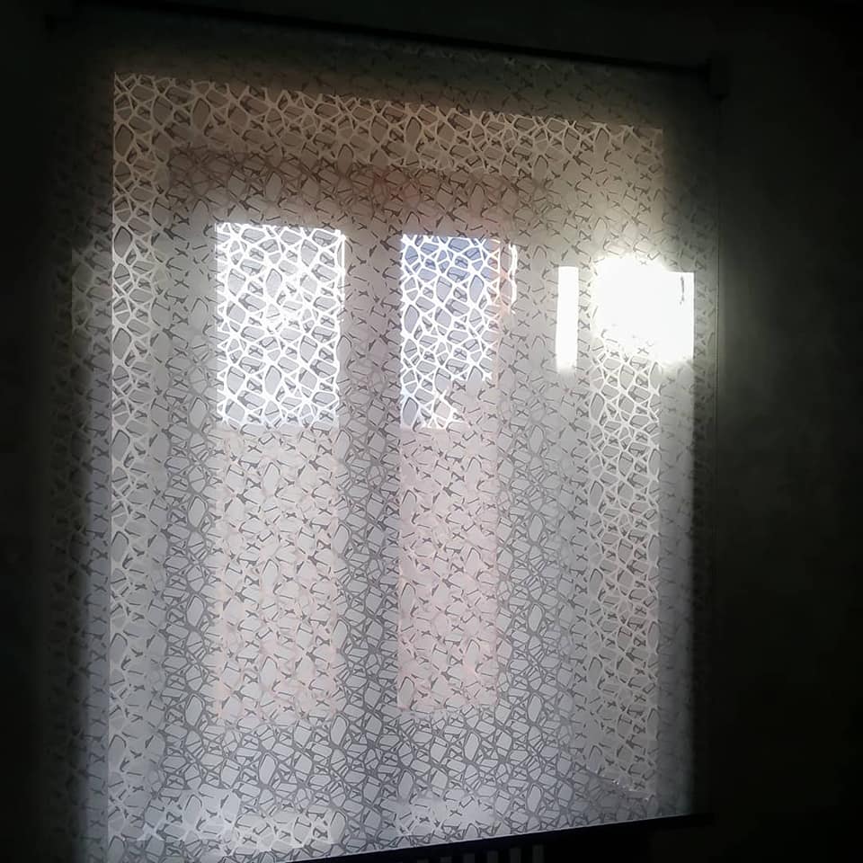 Una tenda trasparente a fantasia copre una finestra luminosa da cui filtra la luce del sole