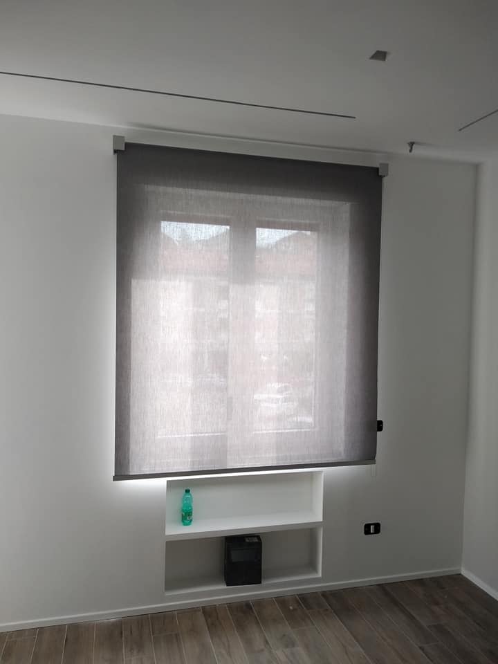 Stanza vuota con una grande tenda grigia, una mensola bianca e un pavimento in legno scuro.