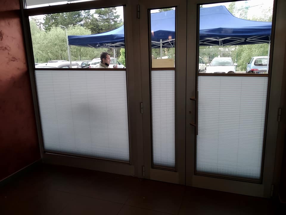 Vista interna attraverso porte a vetri con pannelli inferiori satinati, che si affacciano su tende blu e auto parcheggiate.