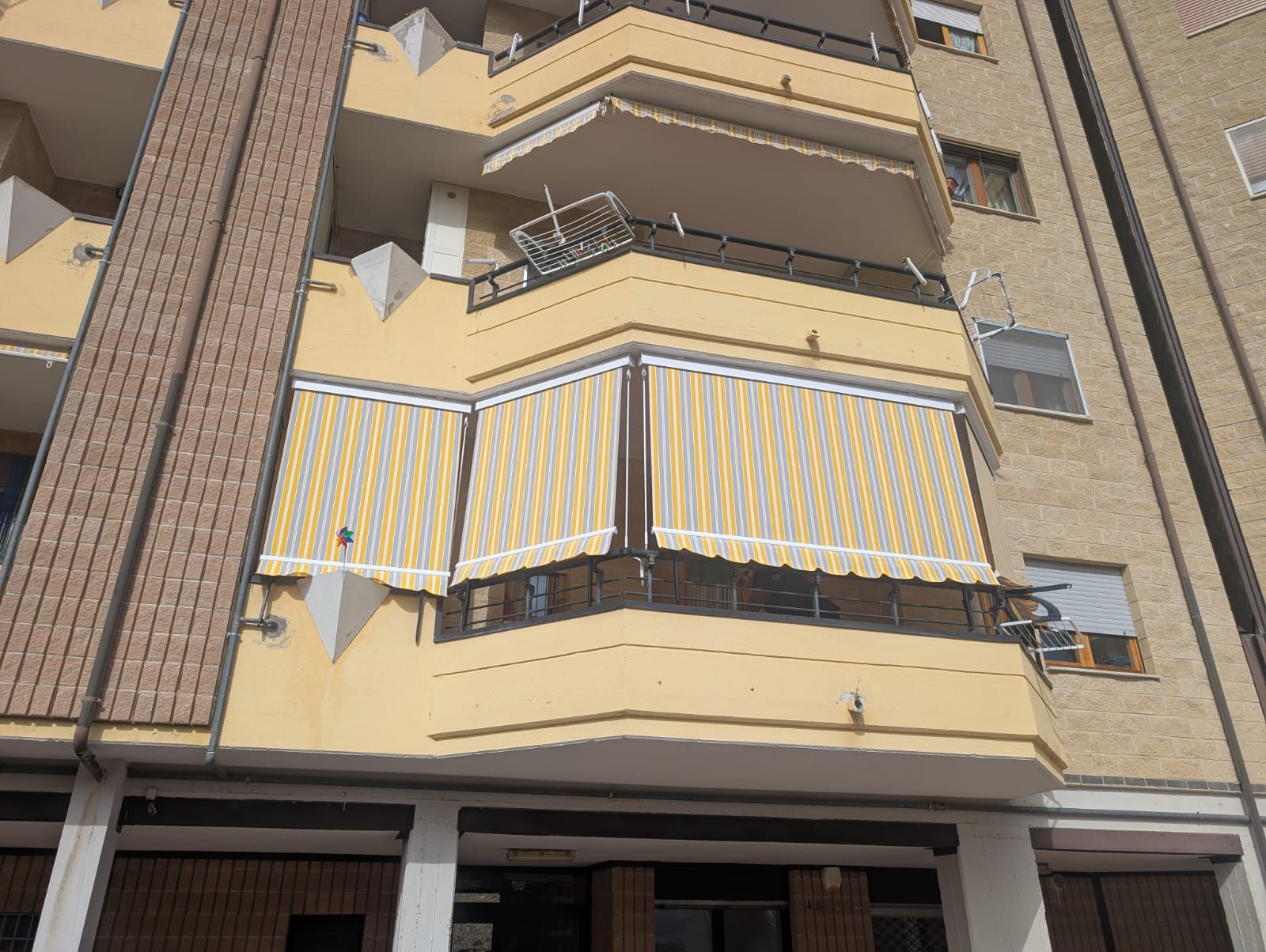 Balcone di un appartamento con tende da sole a strisce gialle e bianche su una facciata beige dell'edificio.