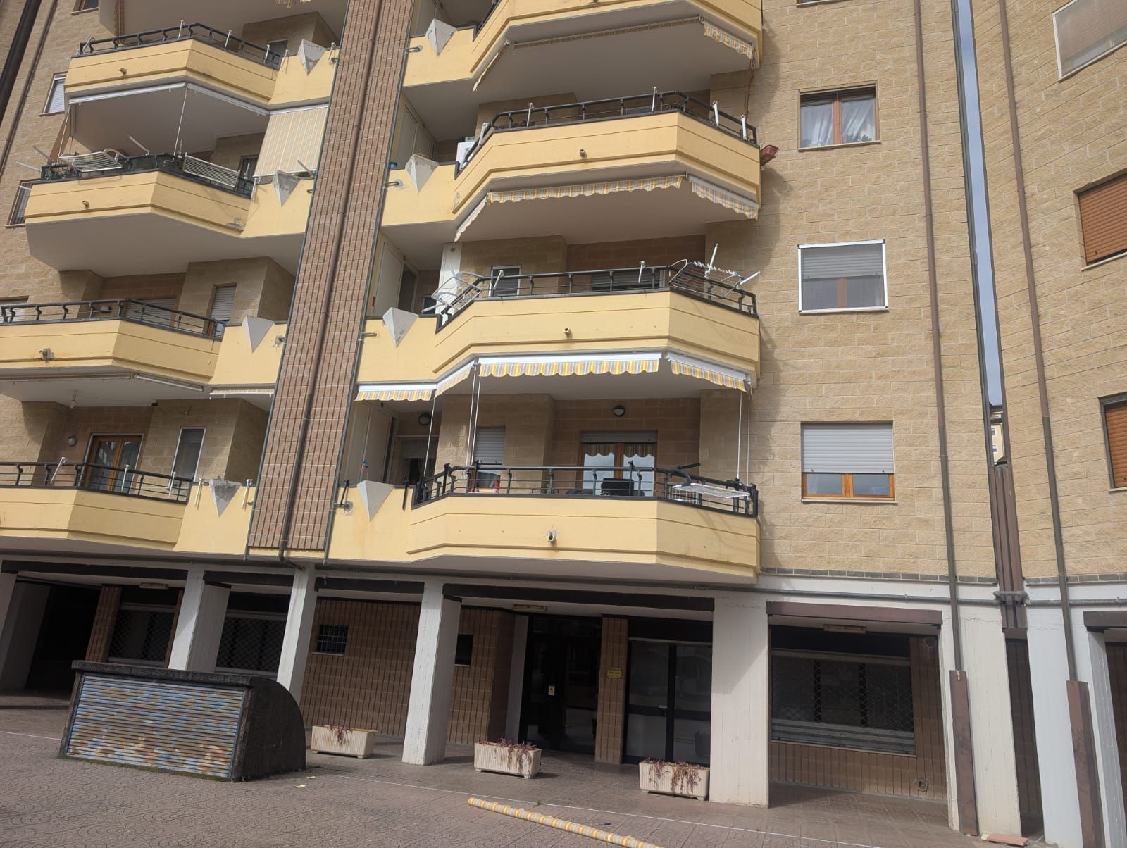 Facciata di un condominio con balconi beige e vetrine al piano terra.