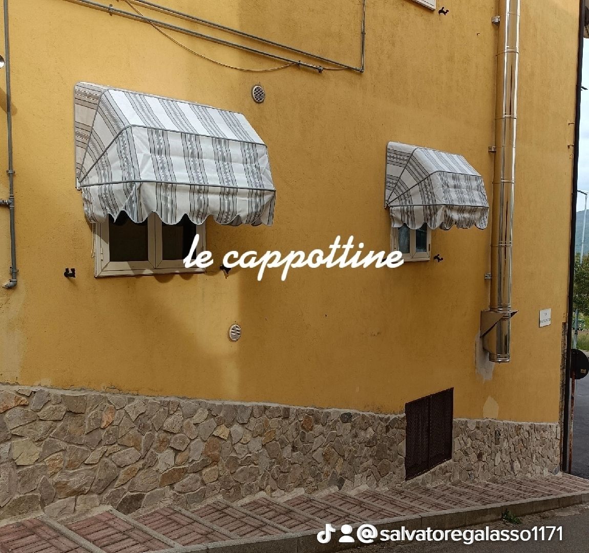 Due tende a strisce bianche su un muro color senape sopra una base in pietra, con la scritta